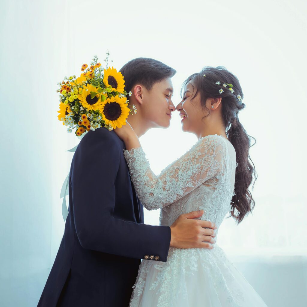 A loving couple at their wedding, kissing tenderly with a sunflower bouquet under soft lighting.