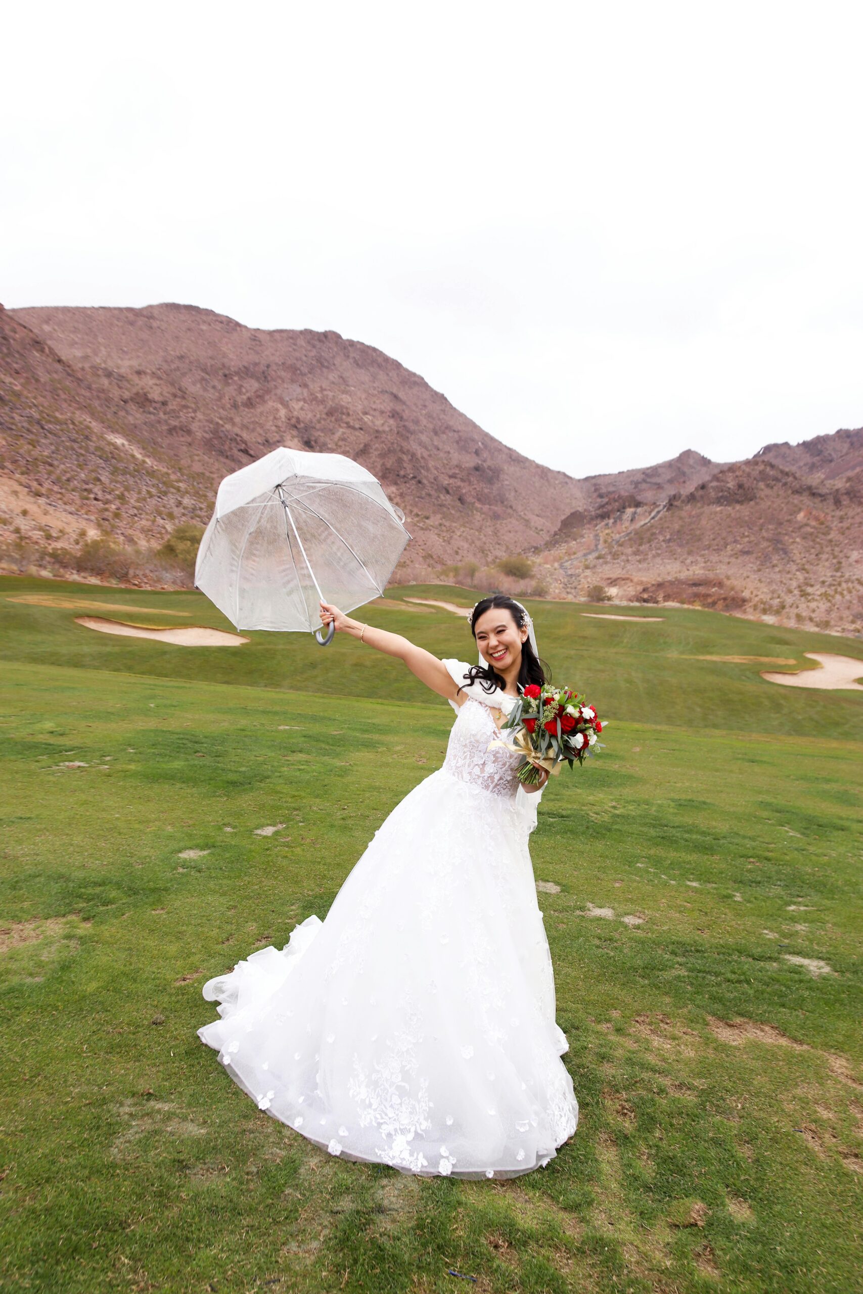 Bride posing outdoors with umbrella, showcasing wedding dress and bouquet.