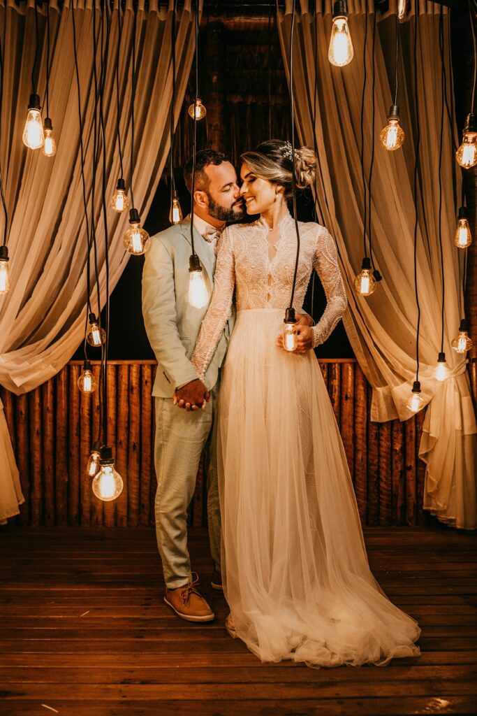 Bride and groom hold hands under hanging lights in an elegant indoor setting.