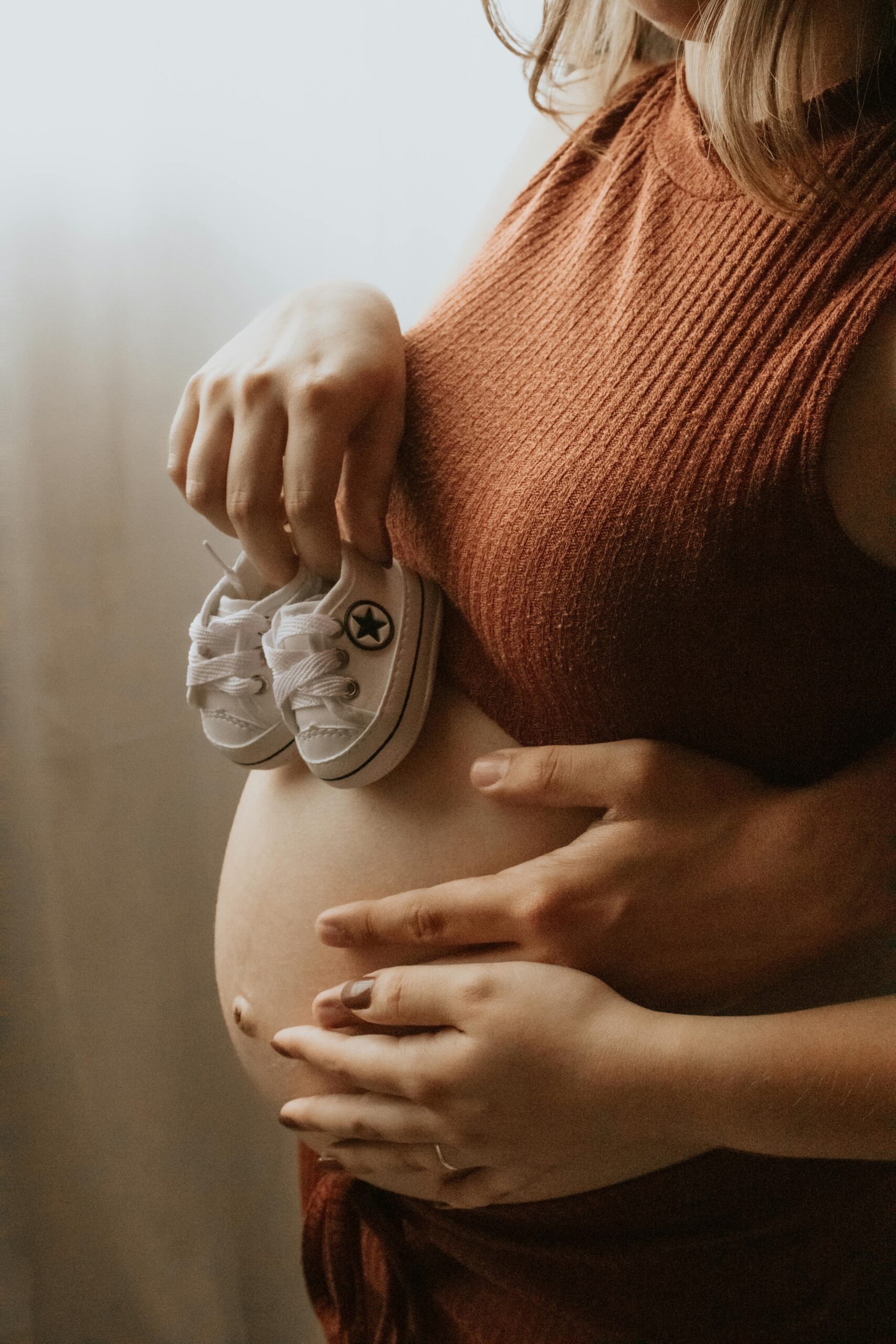 Expecting mother lovingly holds baby shoes on her belly, symbolizing new life.