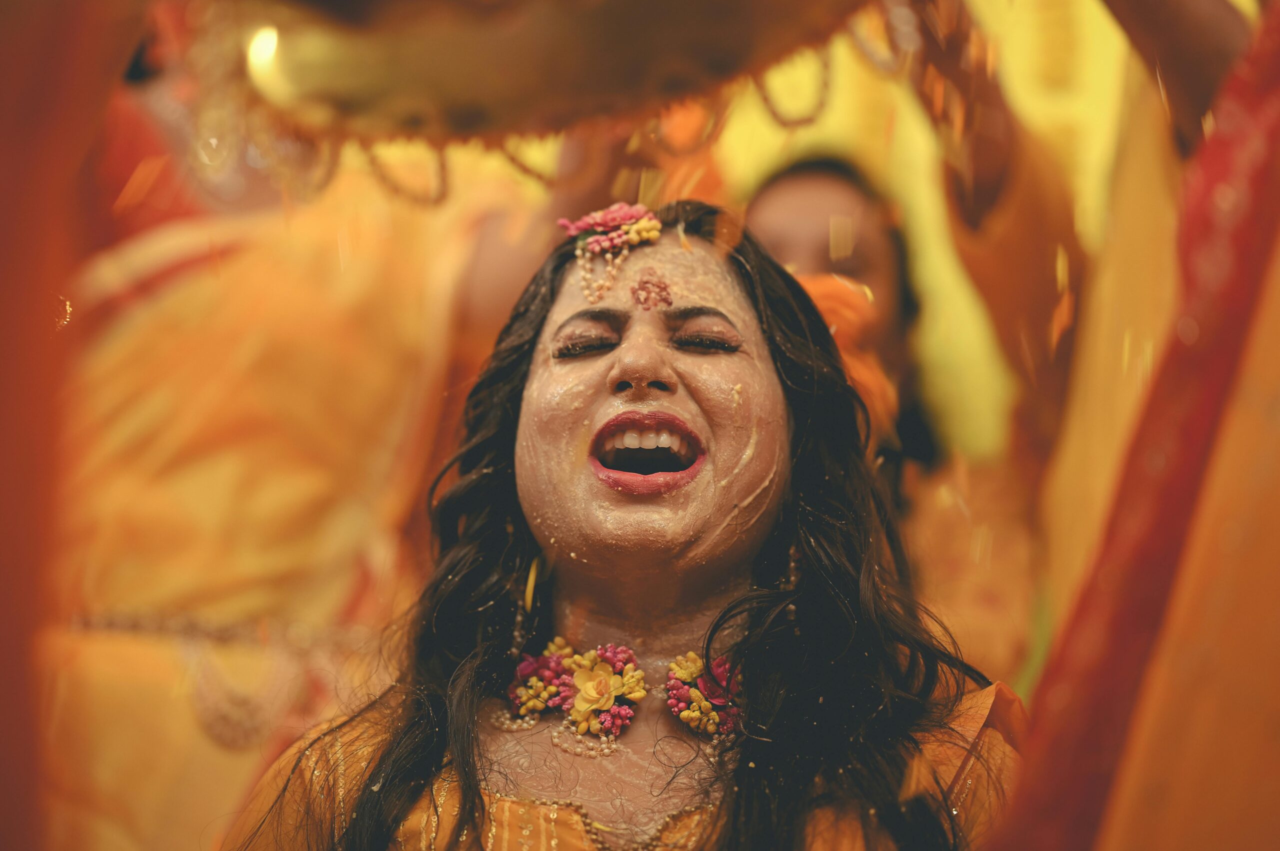 A blissful Indian bride in a vibrant yellow Haldi ceremony with floral decorations.
